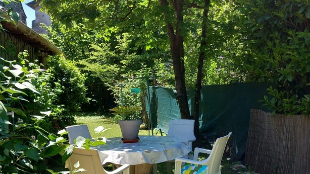 Ein Essbereich im Freien mit Tisch und Stühlen, umgeben von Pflanzen und einem Zaun.