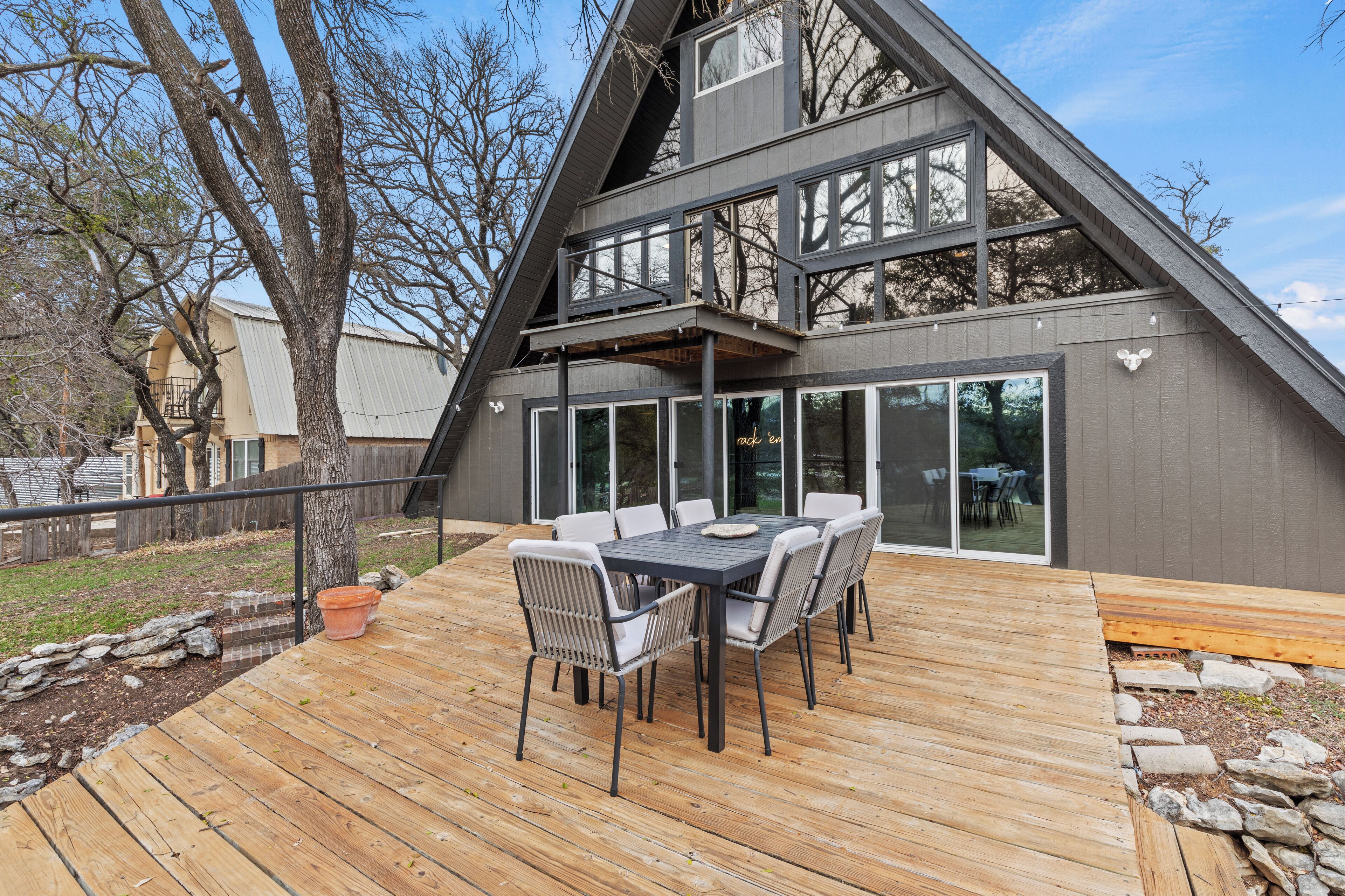 A modern house with a wooden deck, a dining table with chairs, and a large window overlooking the yard.