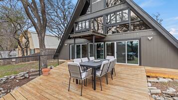 A modern house with a wooden deck, a dining table with chairs, and a large window overlooking the yard.