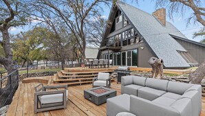 A modern outdoor deck with a stone fire pit, grey sofas, and a barbecue grill.