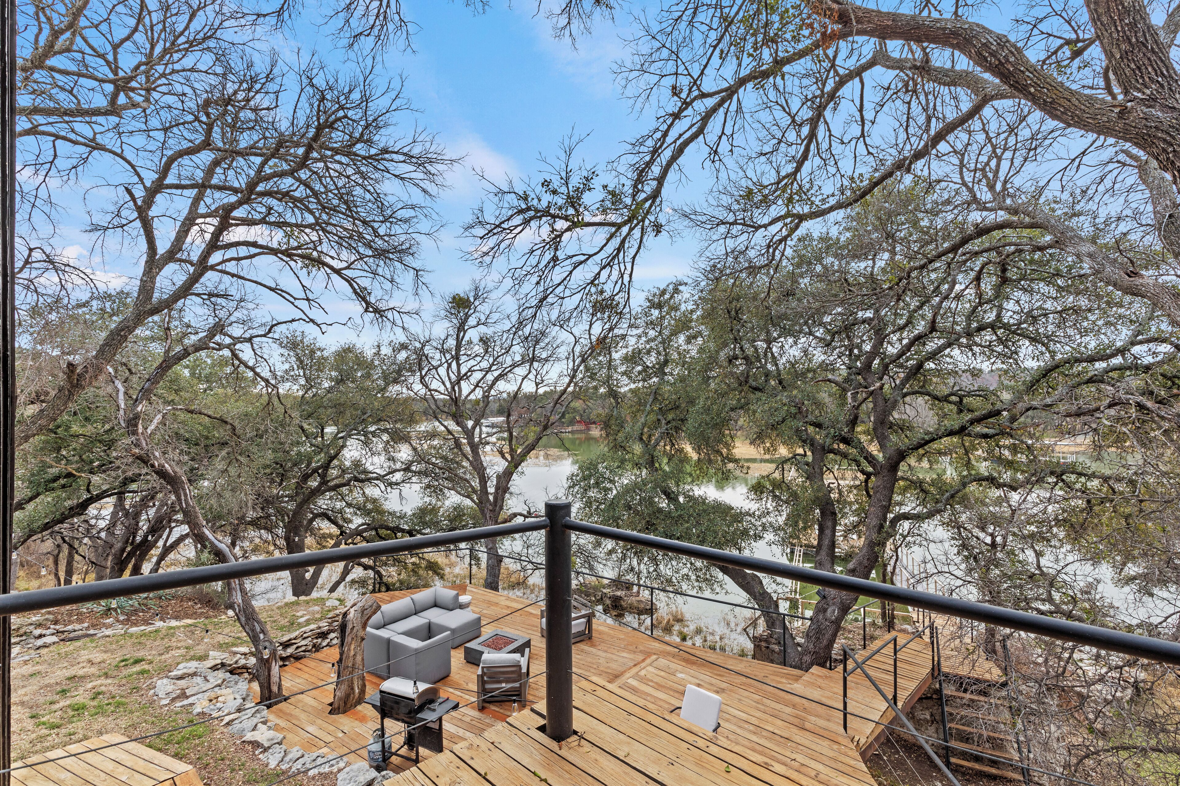 A wooden deck with outdoor furniture, overlooking a lake and surrounded by trees.