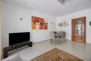 A living room with a flat-screen TV, a dining table with chairs, a wooden door, and a painting on the wall. - Family Apartment in the Historic Center (Lagos)