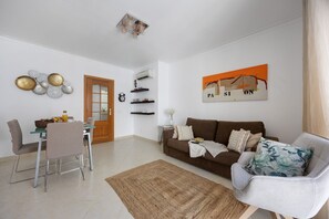 Un salon avec un canapé marron, un fauteuil blanc, une table à manger avec des chaises et une table basse.