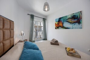 Et soveværelse med seng, lampe, et billede og et vindue med gardiner.