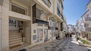 A narrow street with a tiled pavement, a building with a sign 'Orallagos,' and a staircase leading to an entrance.