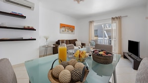 A modern living room with a glass table, bookshelves, a sofa, a TV, and a balcony view.