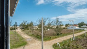 A rural landscape with a dirt road, sparse vegetation, and a few buildings in the distance. - Lofts completos e modernos em Jaguaruna a 50m da Praia - PLO (Jaguaruna)