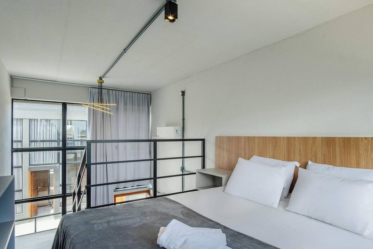 Une chambre d’hôtel moderne équipée d’un lit, d’un bureau, d’une chaise, d’une fenêtre et d’un balcon.