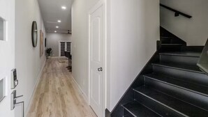 Un couloir doté d’un plancher en bois, de murs blancs et d’un escalier noir.