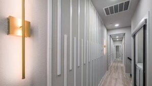 Un couloir moderne avec des panneaux lumineux verticaux, un plancher en bois et une porte en verre au fond.
