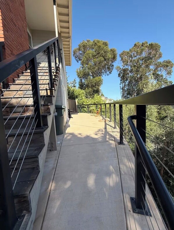 A concrete pathway with a metal railing, leading to a building with a brick facade and a staircase.