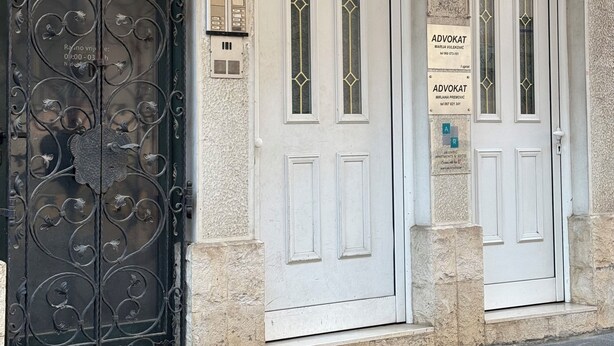 Une façade d’immeuble ornée d’un grand portail en métal travaillé, de deux portes blanches dotées de fenêtres en arc de cercle et d’une enseigne indiquant qu’il s’agit d’un appartement.
