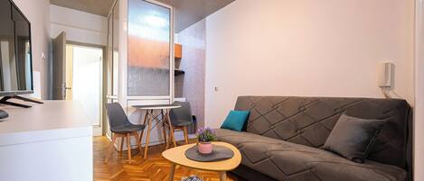 A modern living room with a sofa, a small round table with a plant, and a dining area with chairs and a table.