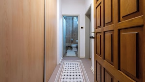 Een smalle gang met houten deuren aan beide kanten, die leidt naar een badkamer met toilet en douche.