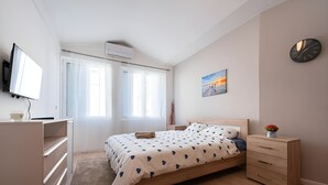 Een slaapkamer met een bed, nachtkastje, televisie en een wandklok.