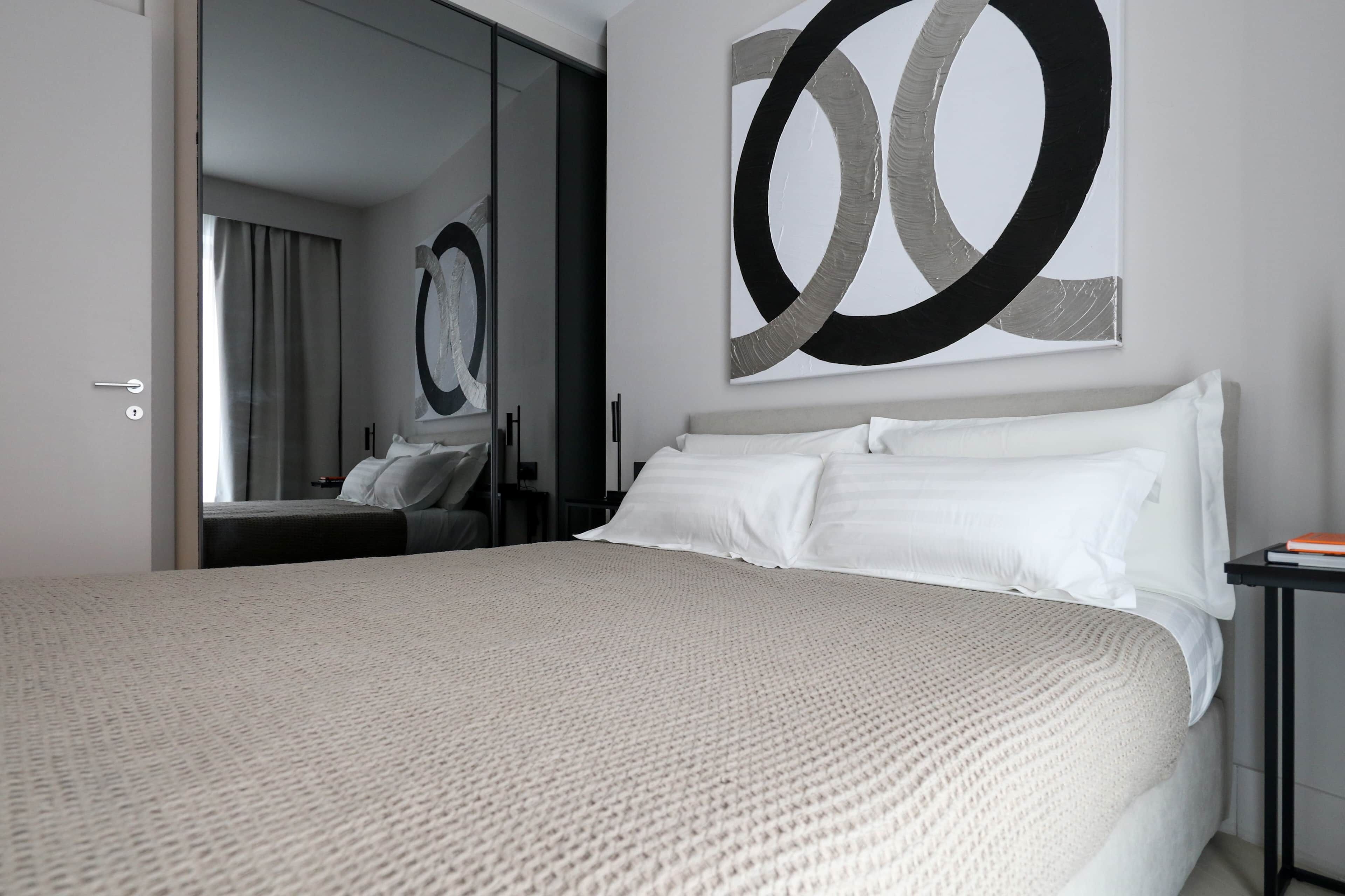 Una camera d'albergo con un letto grande, uno specchio e un quadro astratto moderno appeso al muro.