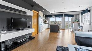A modern kitchen with a flat-screen TV, built-in appliances, and a dining area with a balcony. - Vacation Home 'Santa Divina Relax Para 10 Personas' with Balcony and Wi-Fi (Asturias)