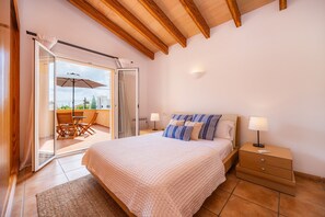 A bedroom with a bed, bedside table, and a view through a sliding glass door to an outdoor seating area.