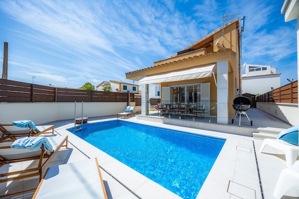 A swimming pool with lounge chairs, a barbecue grill, and a covered patio area.