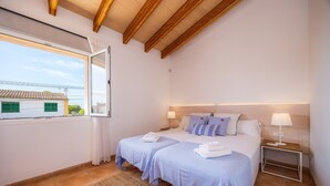 Ein Schlafzimmer mit zwei Betten, einem Fenster, einer Holzbalkendecke und einem Nachttisch mit Lampe.