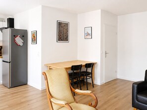 Une cuisine moderne équipée d’un réfrigérateur, d’une table à manger avec des chaises et d’un fauteuil en osier.