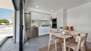 A modern kitchen with white cabinets, stainless steel appliances, and a dining area with wooden chairs and a table. - Sunny Apartments C in Tavira (Tavira)