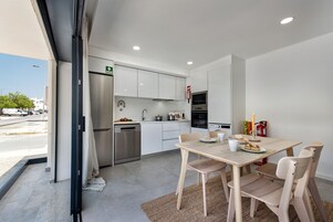 Una cocina moderna con armarios blancos, electrodomésticos de acero inoxidable y un comedor con sillas de madera y una mesa.