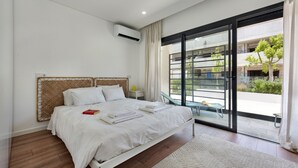 A modern bedroom with a large bed, a glass door leading to an outdoor area, and a built-in air conditioning unit. - Sunny Apartments C in Tavira (Tavira)