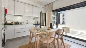 A modern kitchen with white cabinets, a stainless steel refrigerator, and a dining area with wooden chairs and a table.