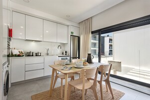 Una cocina moderna con armarios blancos, un refrigerador de acero inoxidable y una zona de comedor con sillas y mesa de madera.