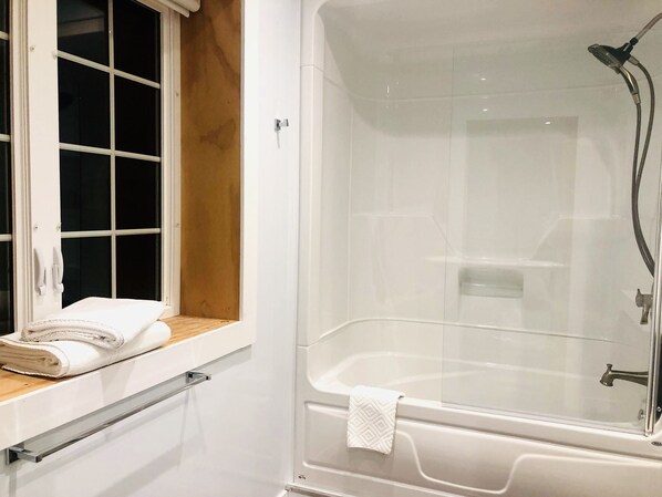 Un baño moderno con ducha de vidrio, una ventana con una toalla en el alféizar y una bañera blanca.