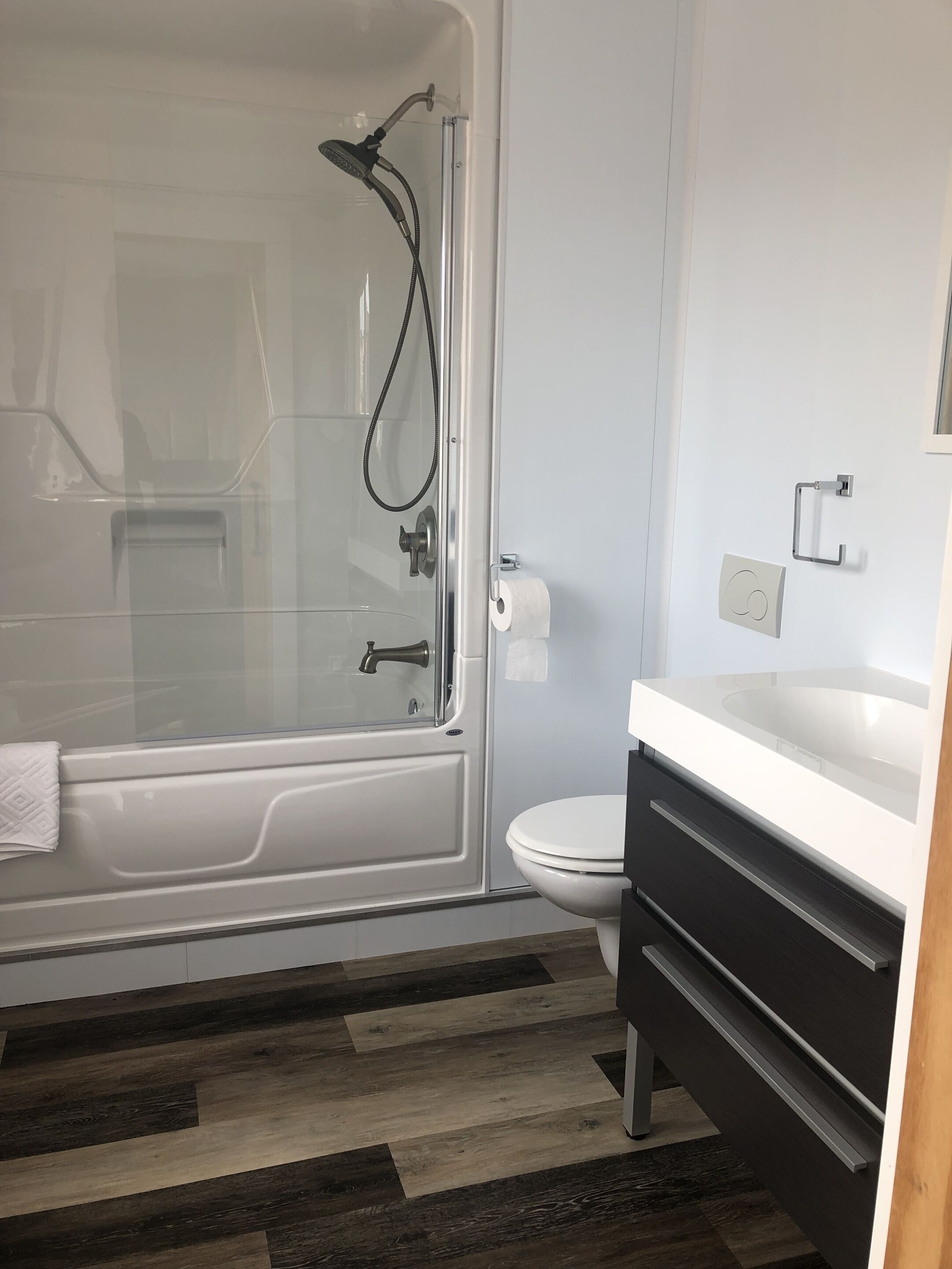 Une salle de bain moderne avec une douche à parois de verre, des toilettes blanches et un meuble-lavabo noir doté de tiroirs.