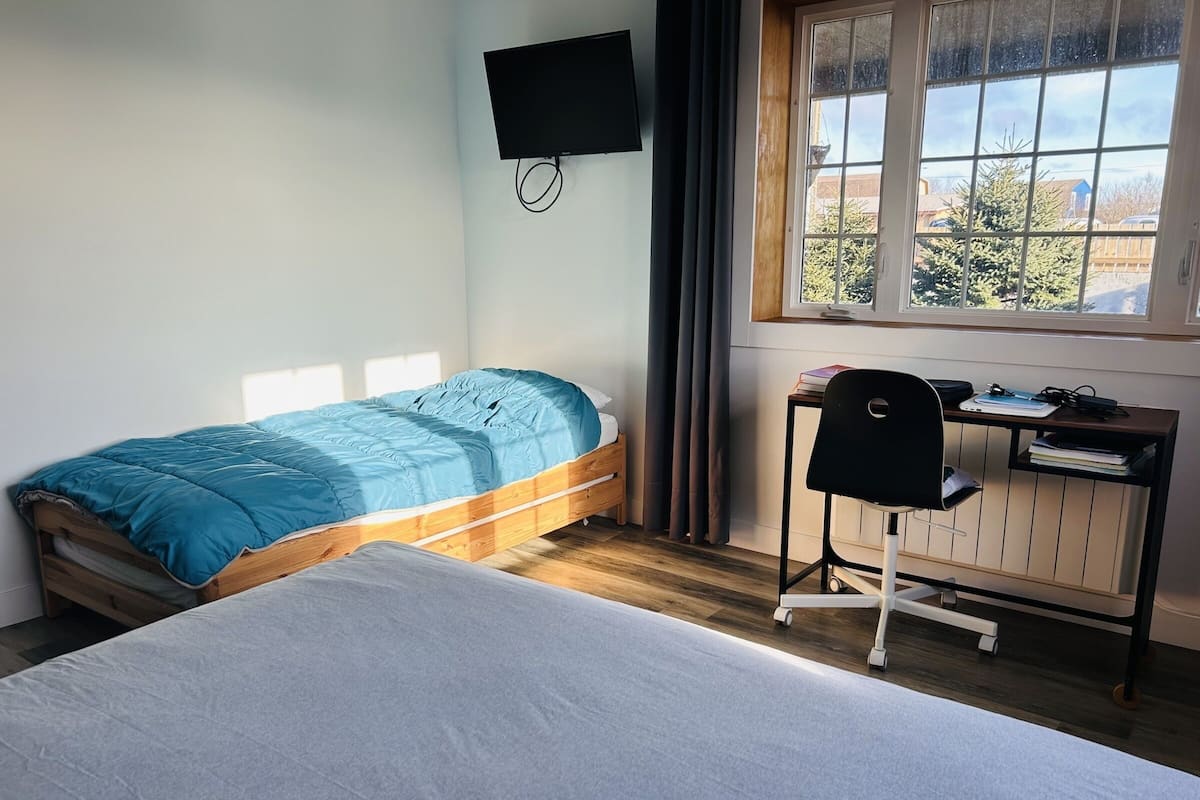 Ein Schlafzimmer mit einem Bett, einem Schreibtisch mit Stuhl, einem Fernseher und einem Fenster mit Blick.