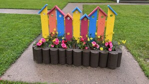 A colorful wooden fence with flower boxes in front of a yellow building. - Au Ptit Kakawi  (Miquelon-Langlade)