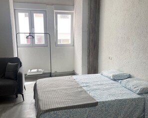 A bedroom with a bed, a chair, a window, and a radiator. - Hospedaje Cartagena (Las Palmas de Gran Canaria)