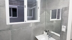 A bathroom with a white sink, wooden cabinet, and a window with a view of another room.