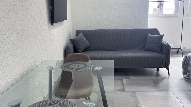 A modern living room with a glass table, a sofa, and a TV mounted on the wall.