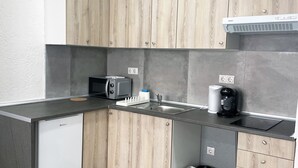 A compact kitchen with a built-in microwave, a coffee maker, and a trash bin.