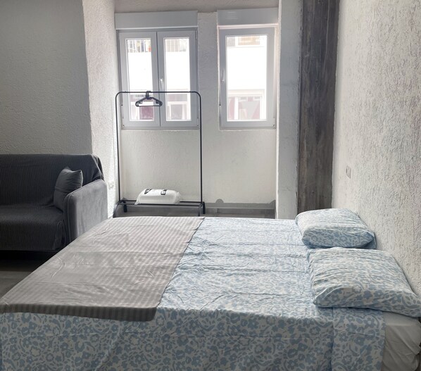 A bedroom with a bed, a sofa, and a window with blinds. - Hospedaje Cartagena (Las Palmas de Gran Canaria)