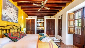 A bedroom with a bed, a ceiling fan, wooden doors, and a large window.