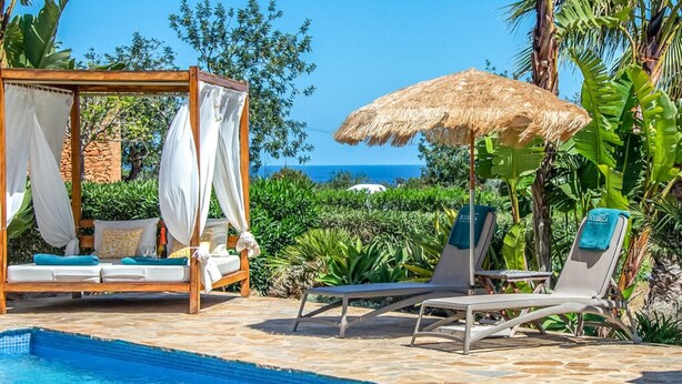A poolside area with a wooden canopy, lounge chairs, and a bed with a canopy.