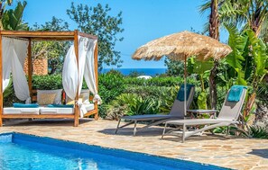Un espace aménagé au bord de la piscine, doté d’un auvent en bois, de chaises longues et d’un lit à baldaquin.