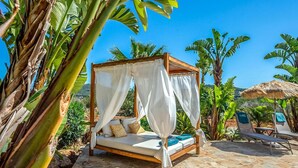 A four-poster bed with white drapes, a stone-tiled patio, and lush tropical plants.