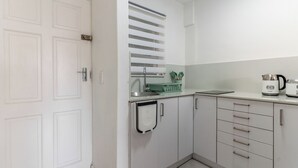 Eine kleine Küche mit weißen Schränken, einem Spülbecken, einem Wasserkocher und einem Utensilienkorb.
