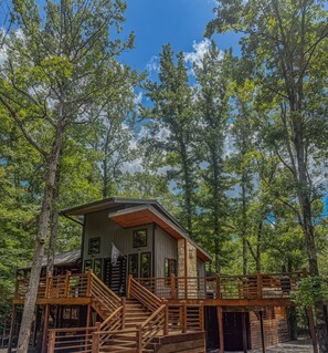 A cabin with a wooden deck and stairs, surrounded by trees.