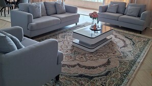 A modern living room with two grey sofas, a coffee table, and a patterned rug. -  Panoramic Ocean Views | 3BR on 7th Floor | Rooftop Pool & Gym — Nyali (Mombasa)