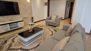 Una sala de estar moderna con un televisor de pantalla plana grande, un sofá gris, un tapete estampado y una mesa de centro con un jarrón de flores.