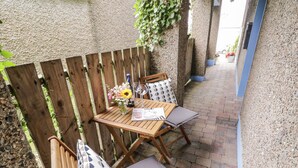 An outdoor patio with a wooden table and chairs, a vase with flowers, and a brick pathway. - The Burma (Letterkenny)