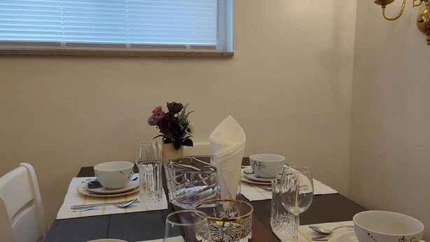 Een eettafel gedekt met witte borden, kommen en glazen, met een bloevas en een kaars op tafel.
