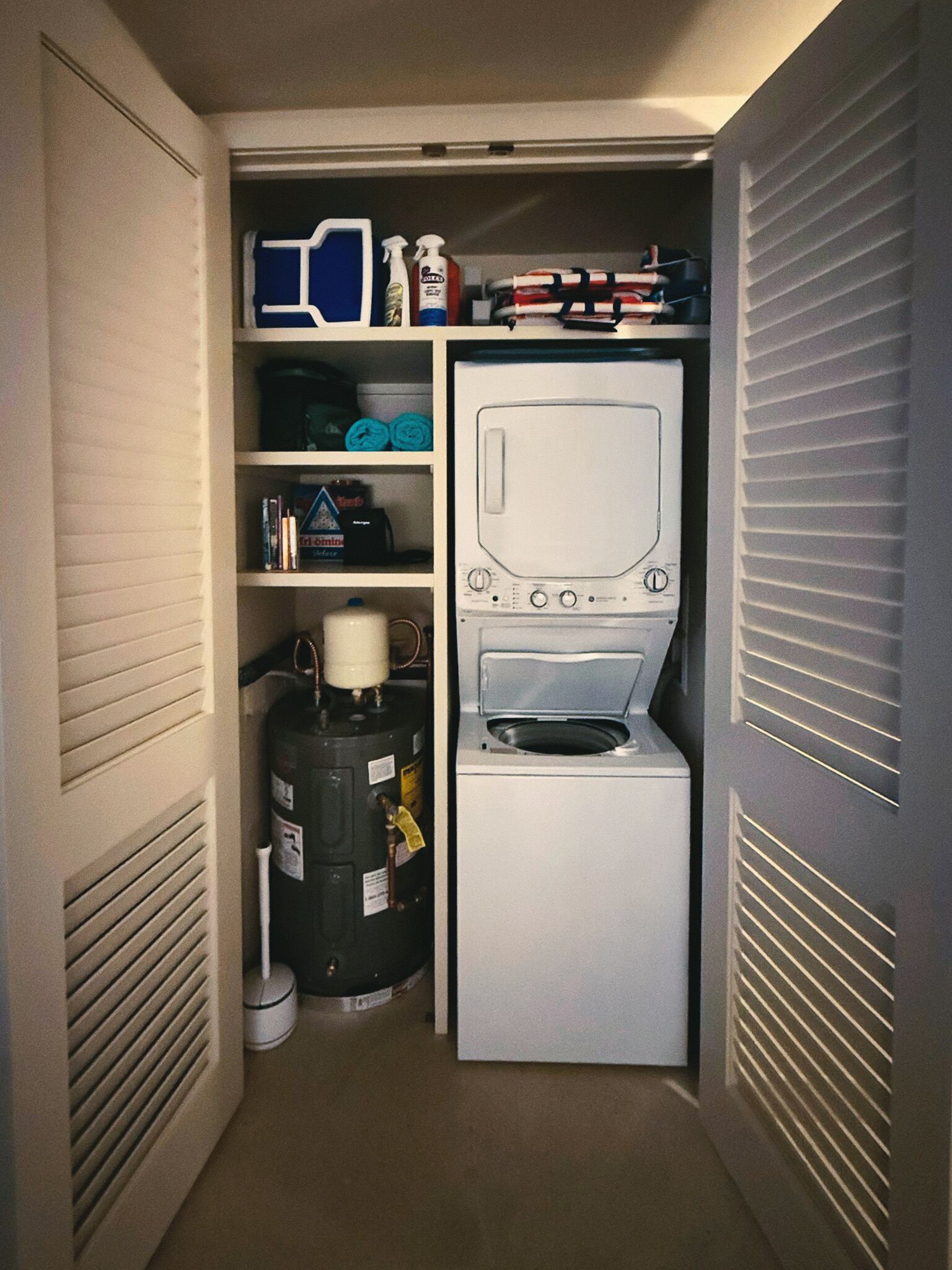 A compact laundry room with a washer and dryer, a water heater, and storage shelves.